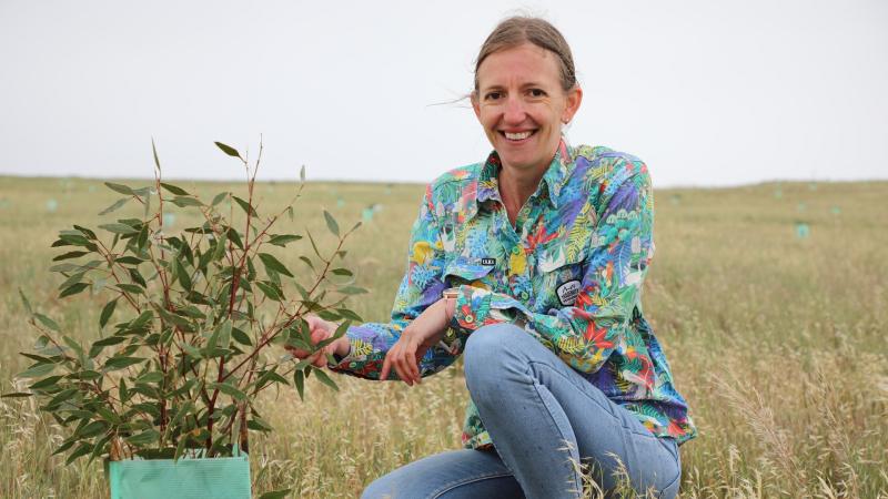 Holly squatting down next to a native tree planting