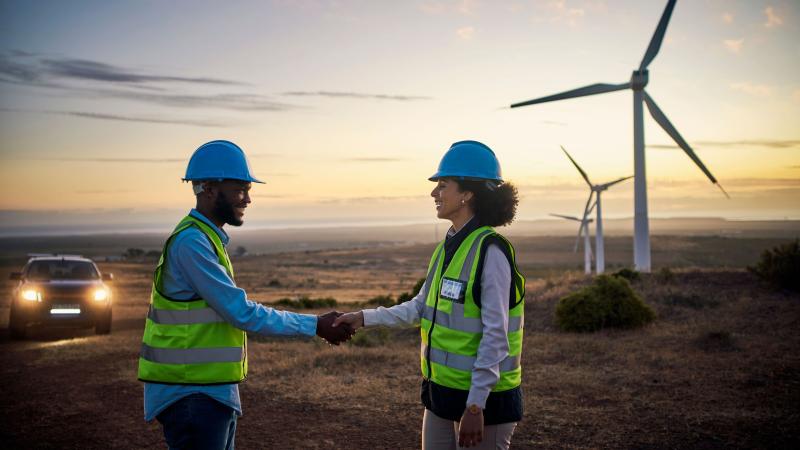 Photo of engineers shaking hands in front of wind turbines